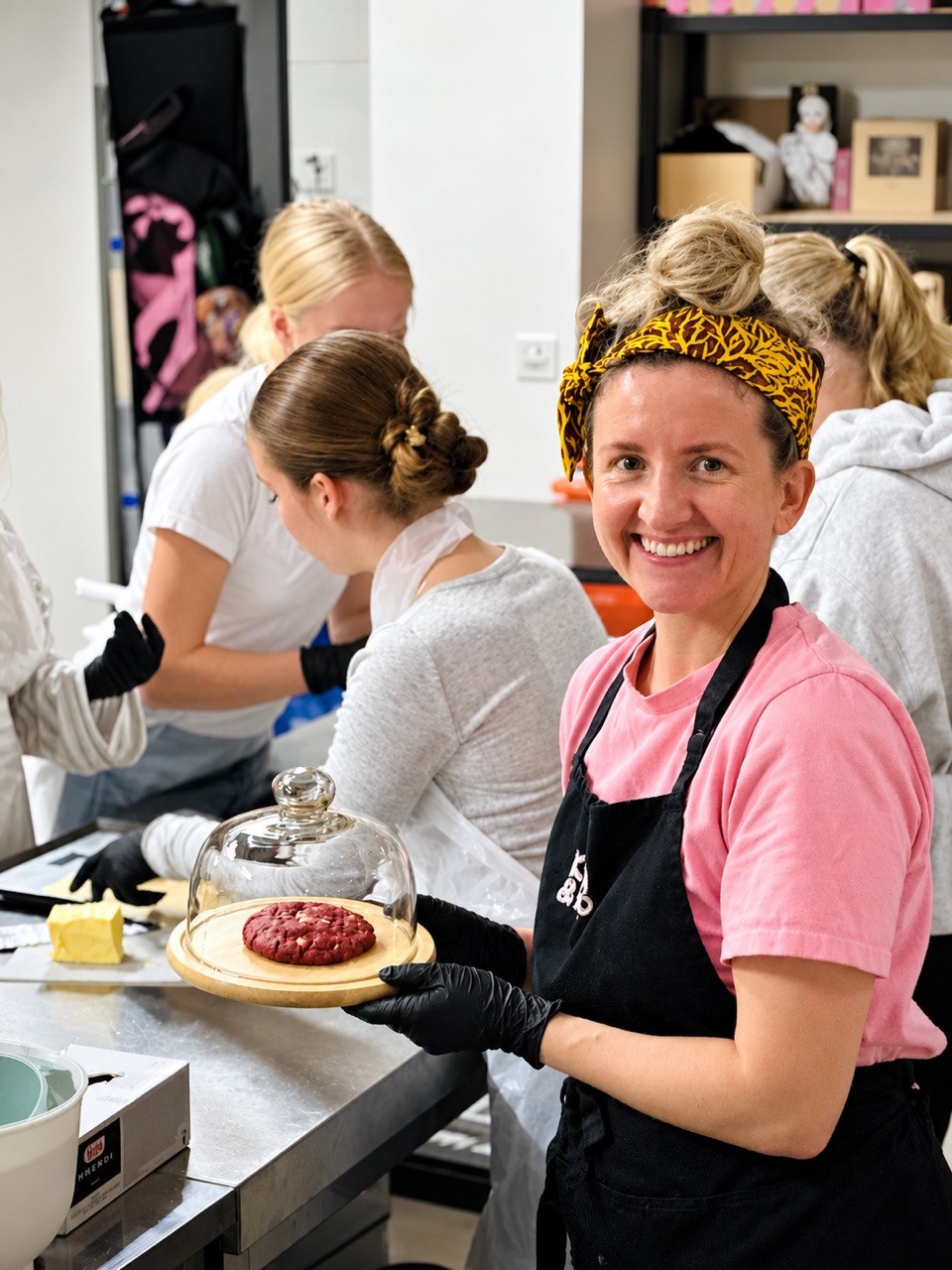 A smiling guest holding a freshly baked red velvet cookie under a glass dome during a cookie-making session in our kitchen